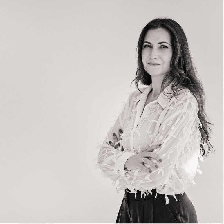 Dziewczyna stoi z założonymi rękoma, za nią jednolite tło